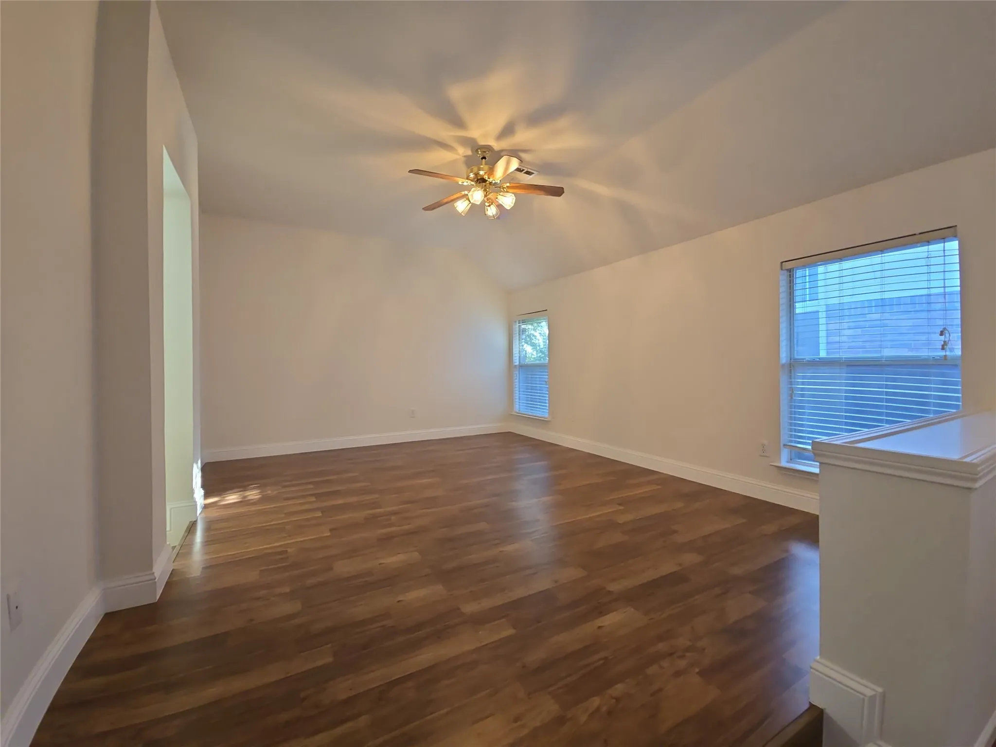 Vaulted ceiling with a ceiling fan light fixture, wood-finish flooring, and two windows