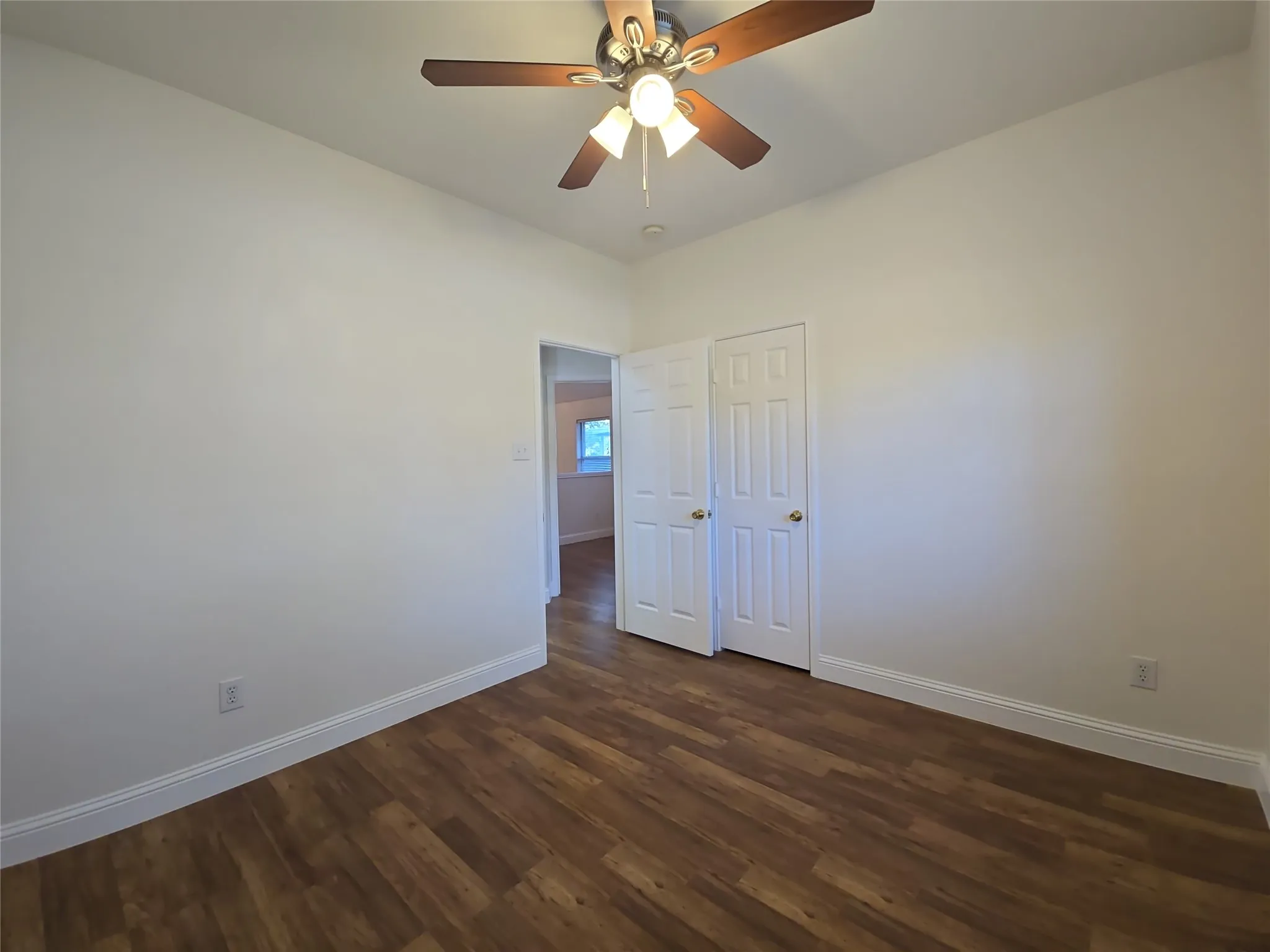 Wood-finish flooring, white walls, ceiling fan with integrated lighting, and white bi-fold closet doors