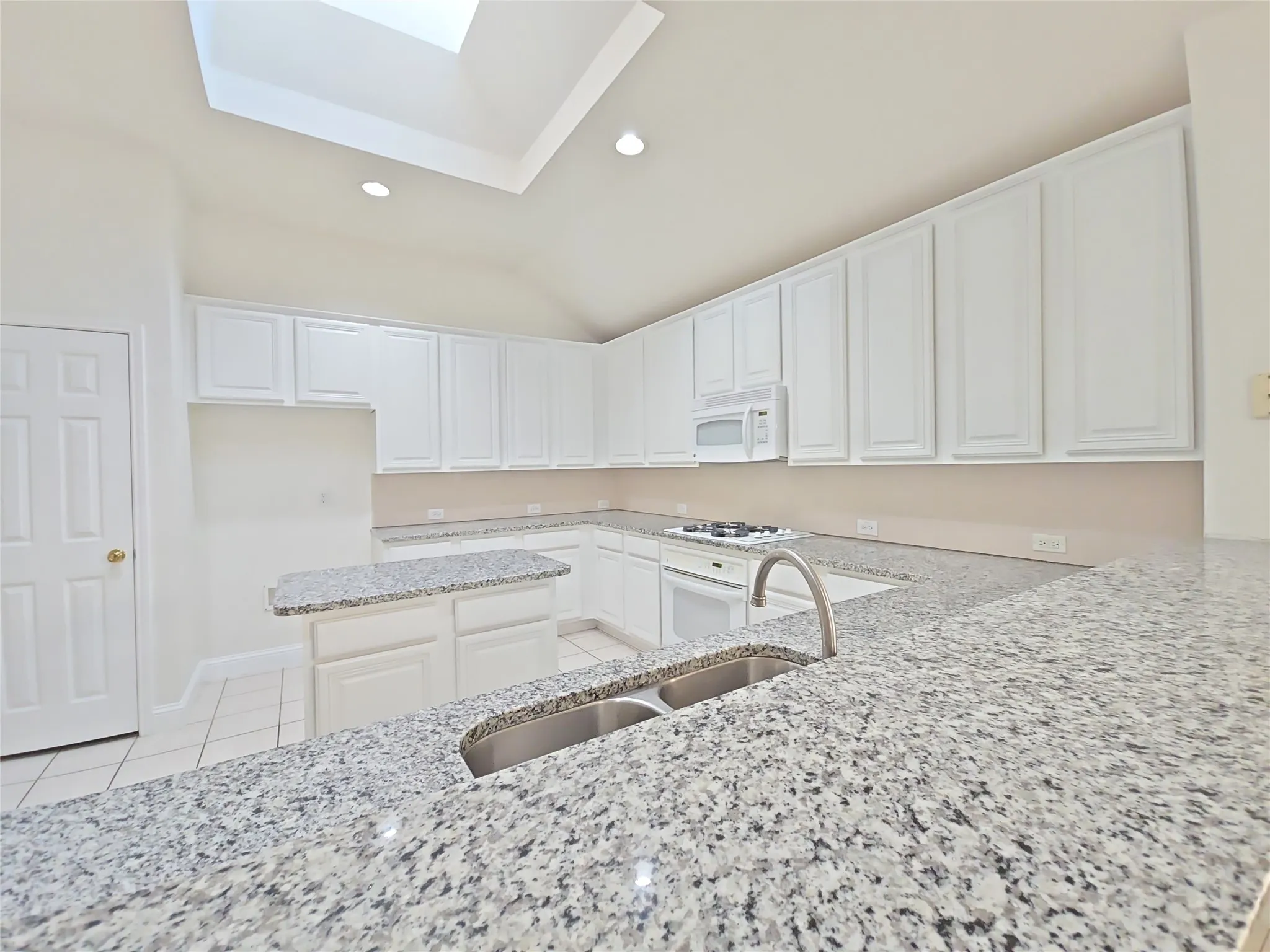 Kitchen featuring granite countertops, white cabinetry, a dual basin stainless steel sink, and a skylight