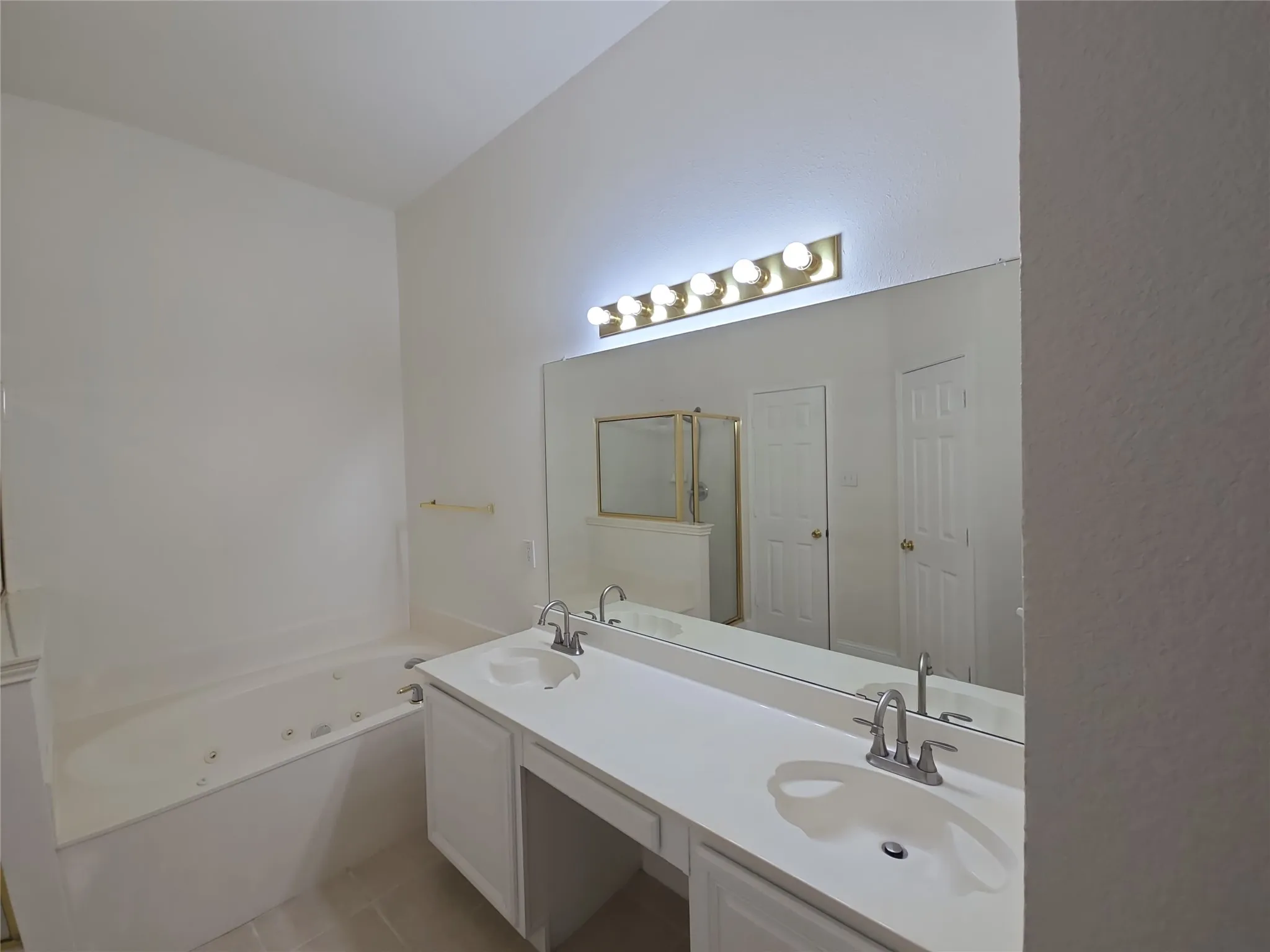 Dual vanity with undermount sinks, expansive mirror, vanity lighting, built-in cabinetry, and a jetted soaking tub