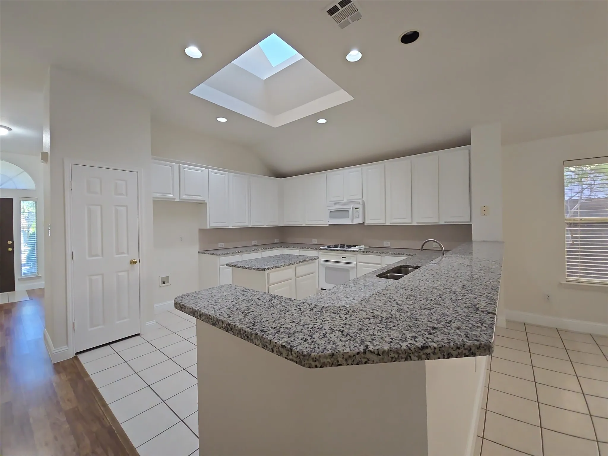 Kitchen featuring white cabinetry, granite countertops, tile flooring, a built-in microwave, and a skylight