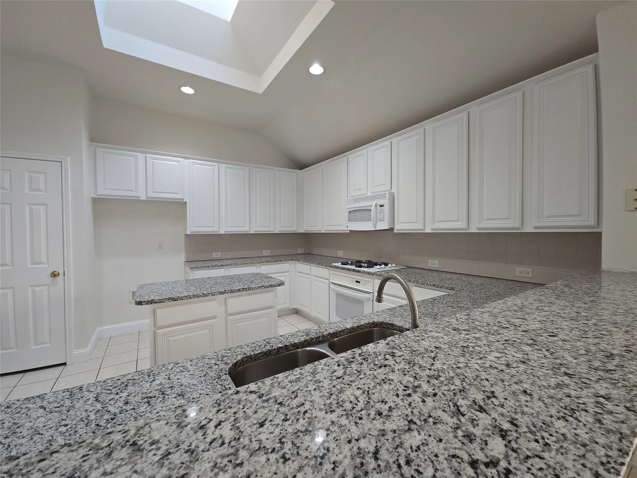 Spacious kitchen featuring extensive granite countertops, white cabinetry, a skylight, recessed lighting, and a center island