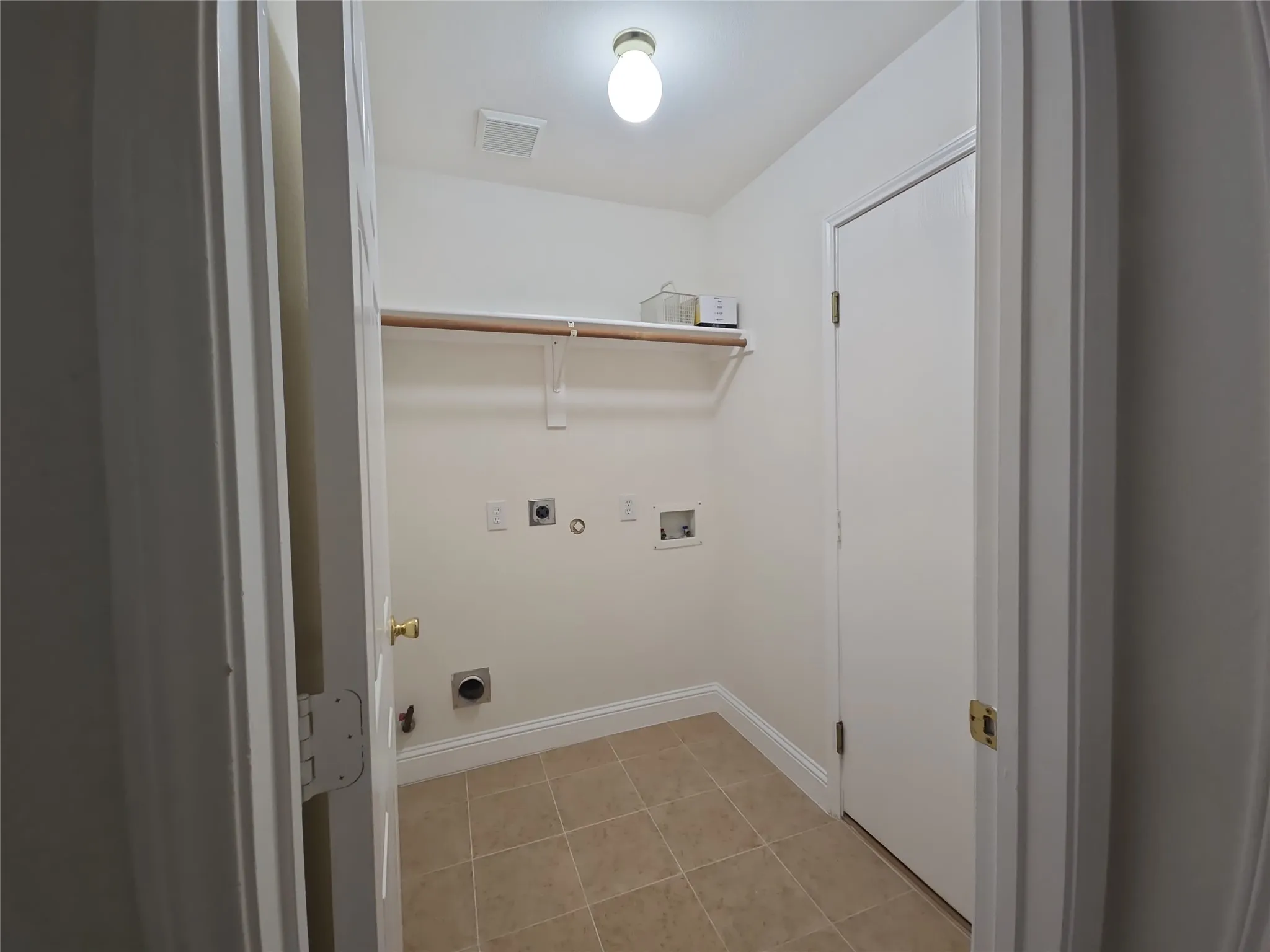 Utility room with neutral tile flooring, a wall-mounted shelf, and laundry hookups