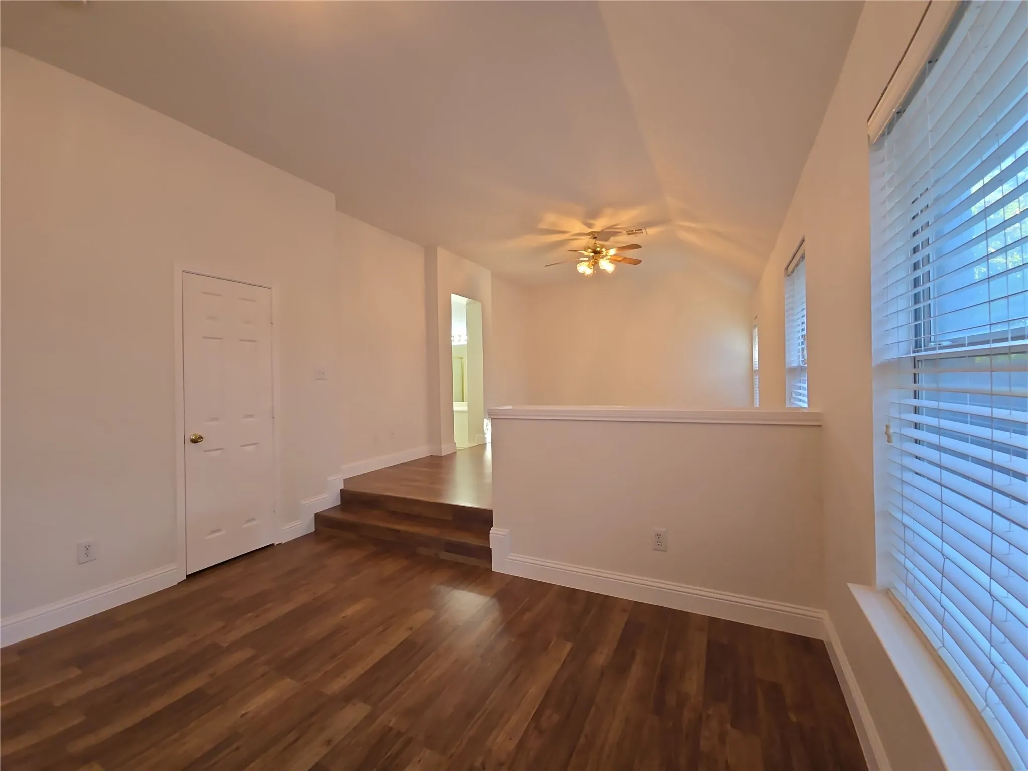 Vaulted ceiling with a ceiling fan, wood-finish flooring, multiple windows with blinds, and an interior door