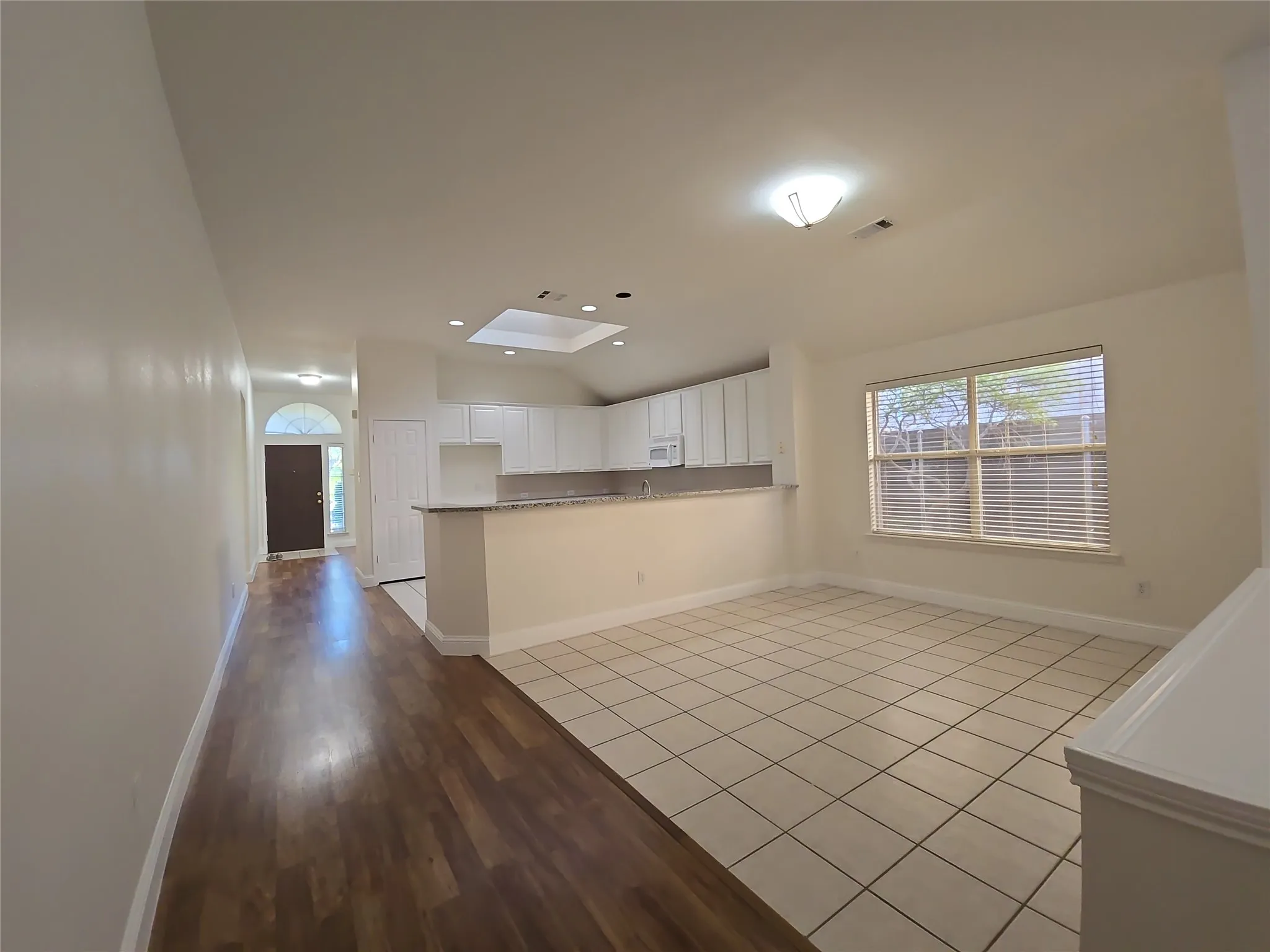Combined flooring surfaces, vaulted ceiling, kitchen pass-through, skylight, and window with horizontal blinds