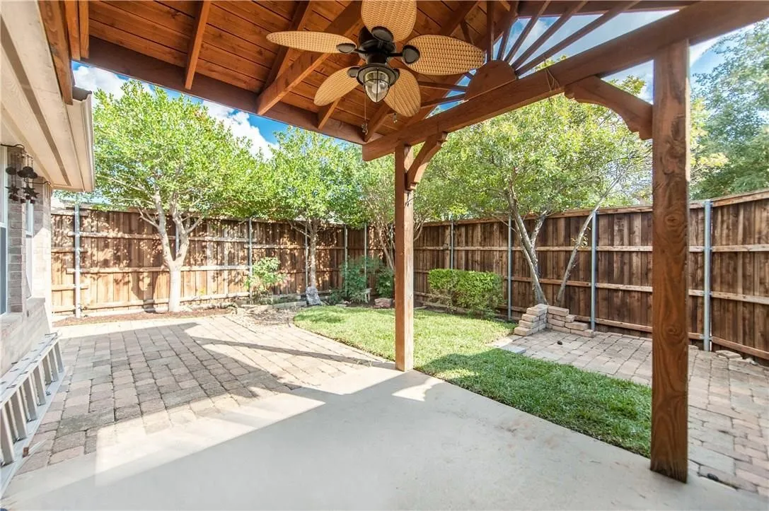 Covered patio with a ceiling fan, concrete and paver flooring, wood privacy fencing, and a manicured lawn