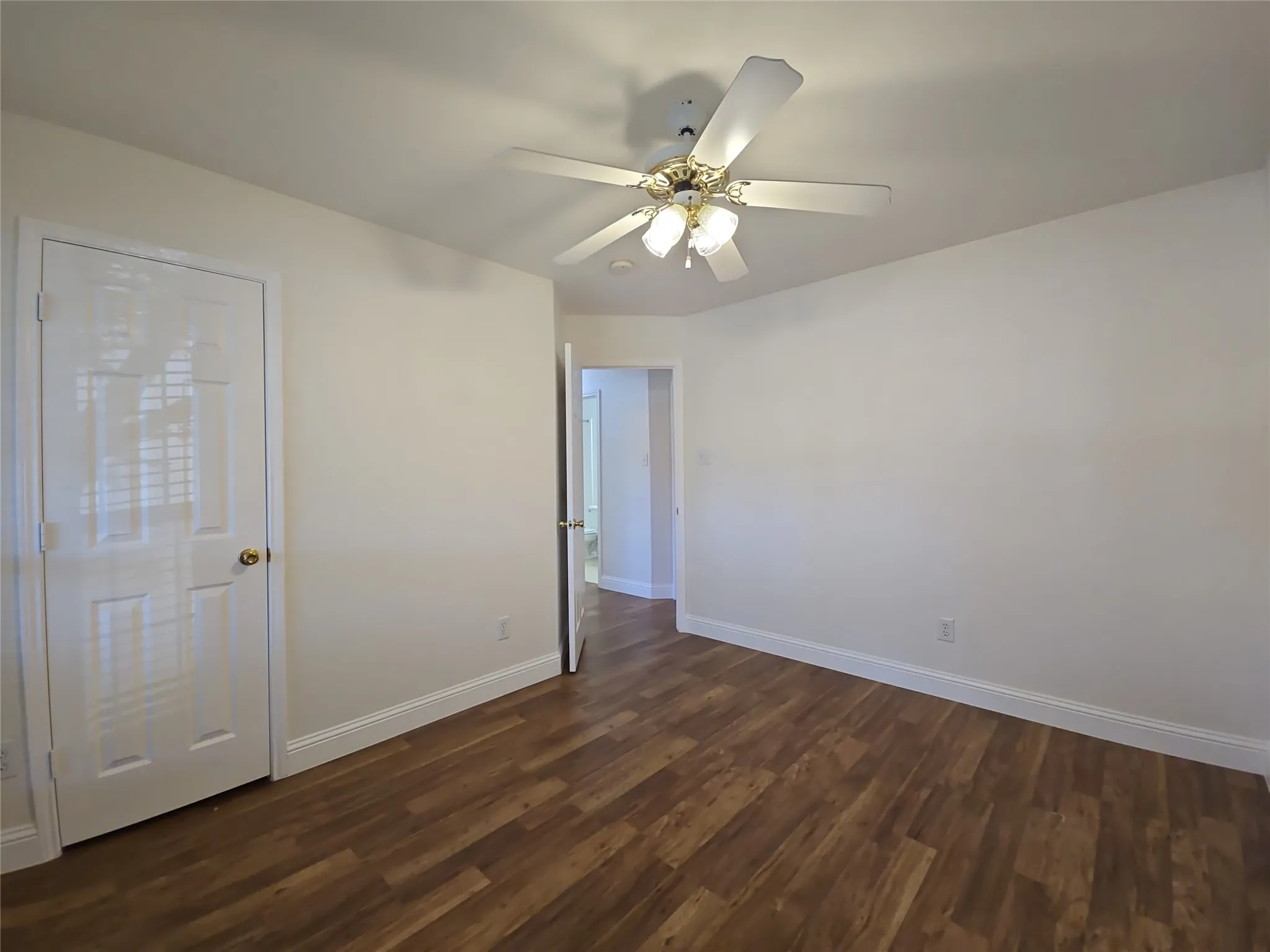 Wood-finish flooring, white walls, white trim, and a ceiling fan with integrated lighting
