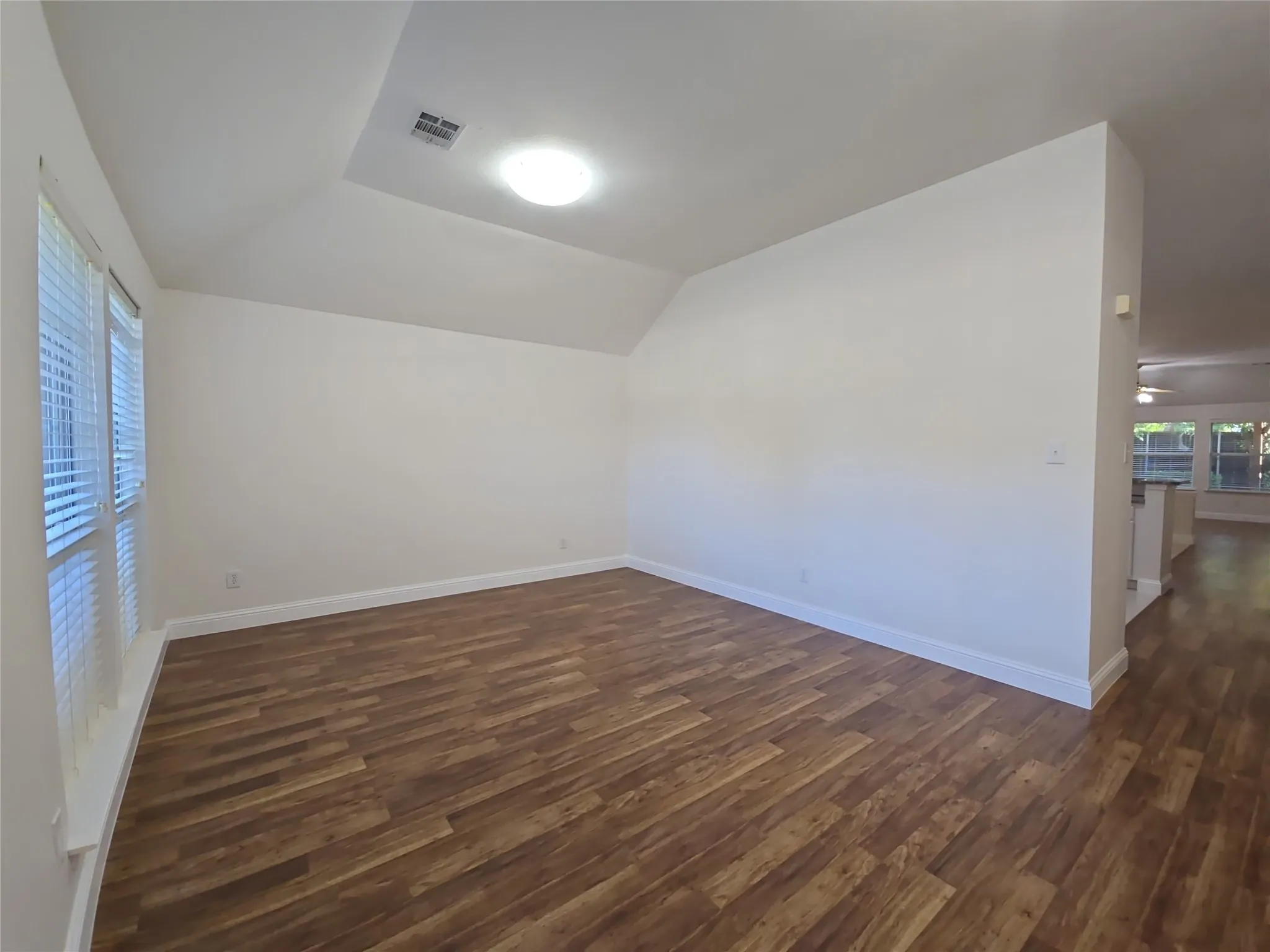 Vaulted ceiling with an integrated light fixture, wood-finish flooring, and multiple windows with blinds