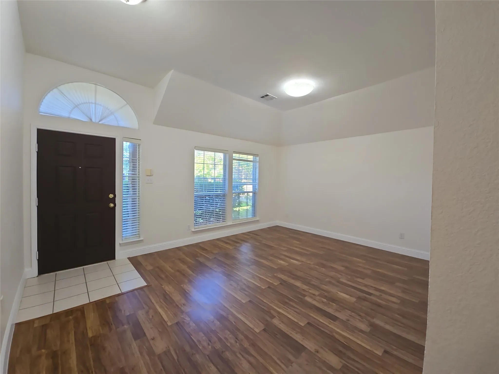 Wood-finish flooring, vaulted ceiling, and multiple windows with blinds