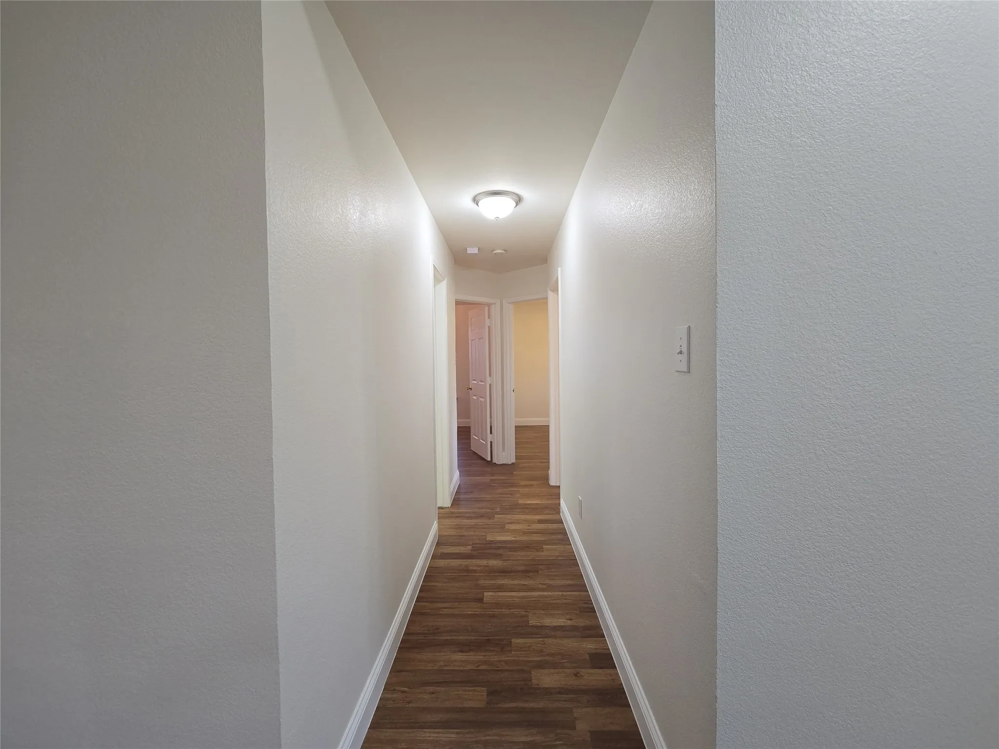 Hallway featuring wood-finish flooring, light neutral paint, and a ceiling-mounted light fixture