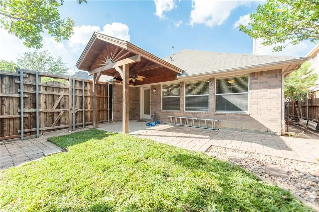 Brick exterior with multiple windows, covered patio featuring a ceiling fan, paved patio area, and a wood privacy fence