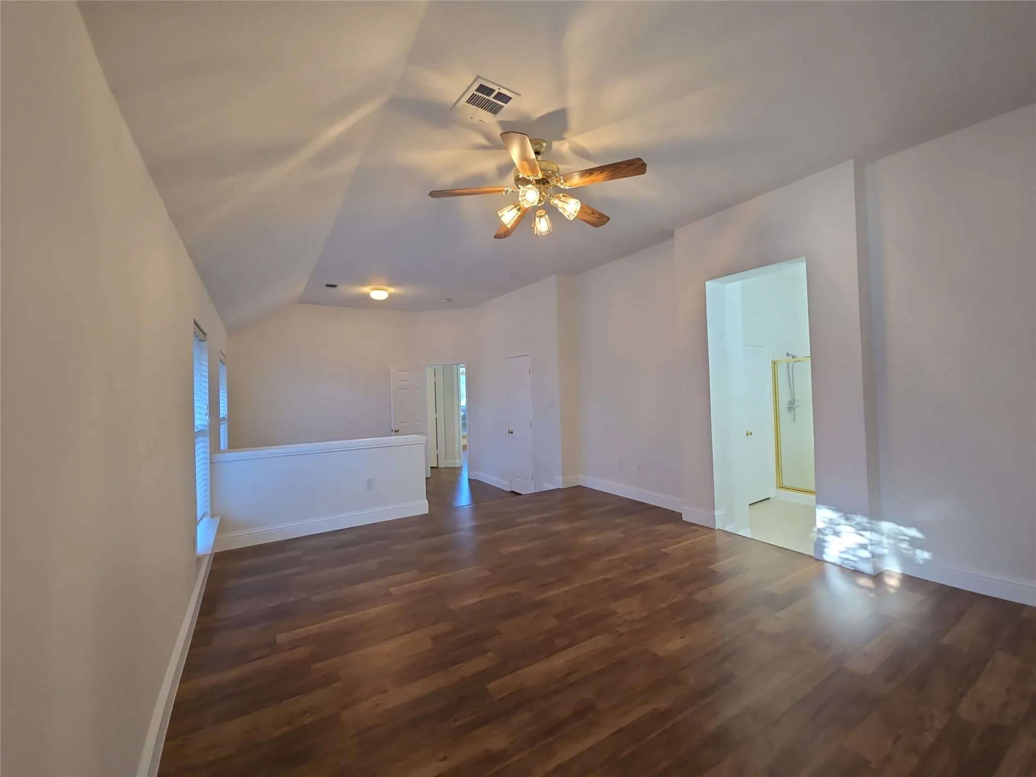 Wood-finish flooring, vaulted ceiling, ceiling fan, white interior paint, and a half-wall partition