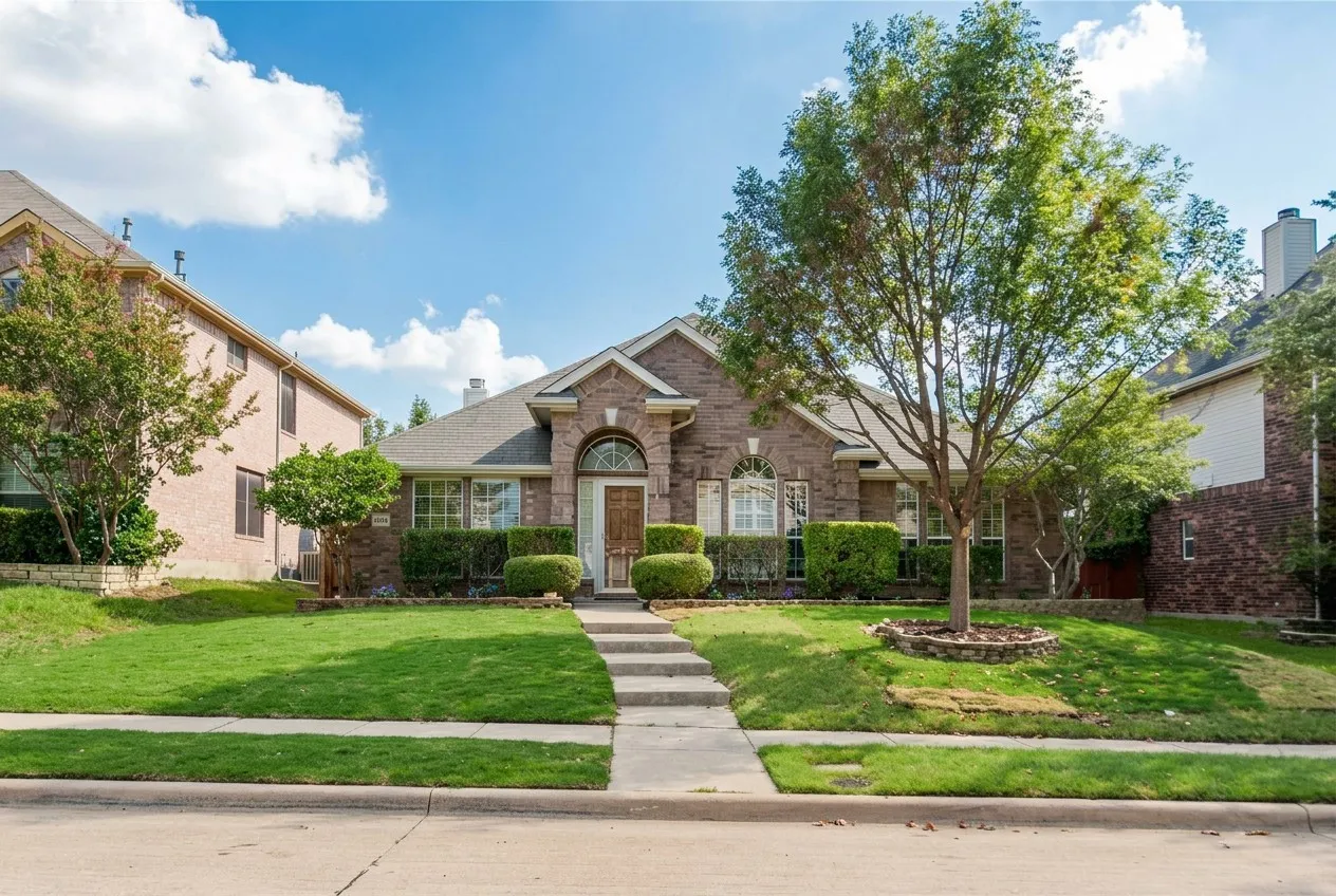 Brick exterior with an arched entry, manicured landscaping, mature trees, and a concrete walkway