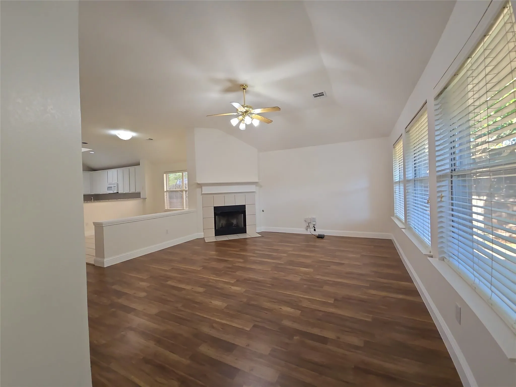 Vaulted ceiling with a ceiling fan, wood-finish flooring, and a fireplace with a tile surround and mantel