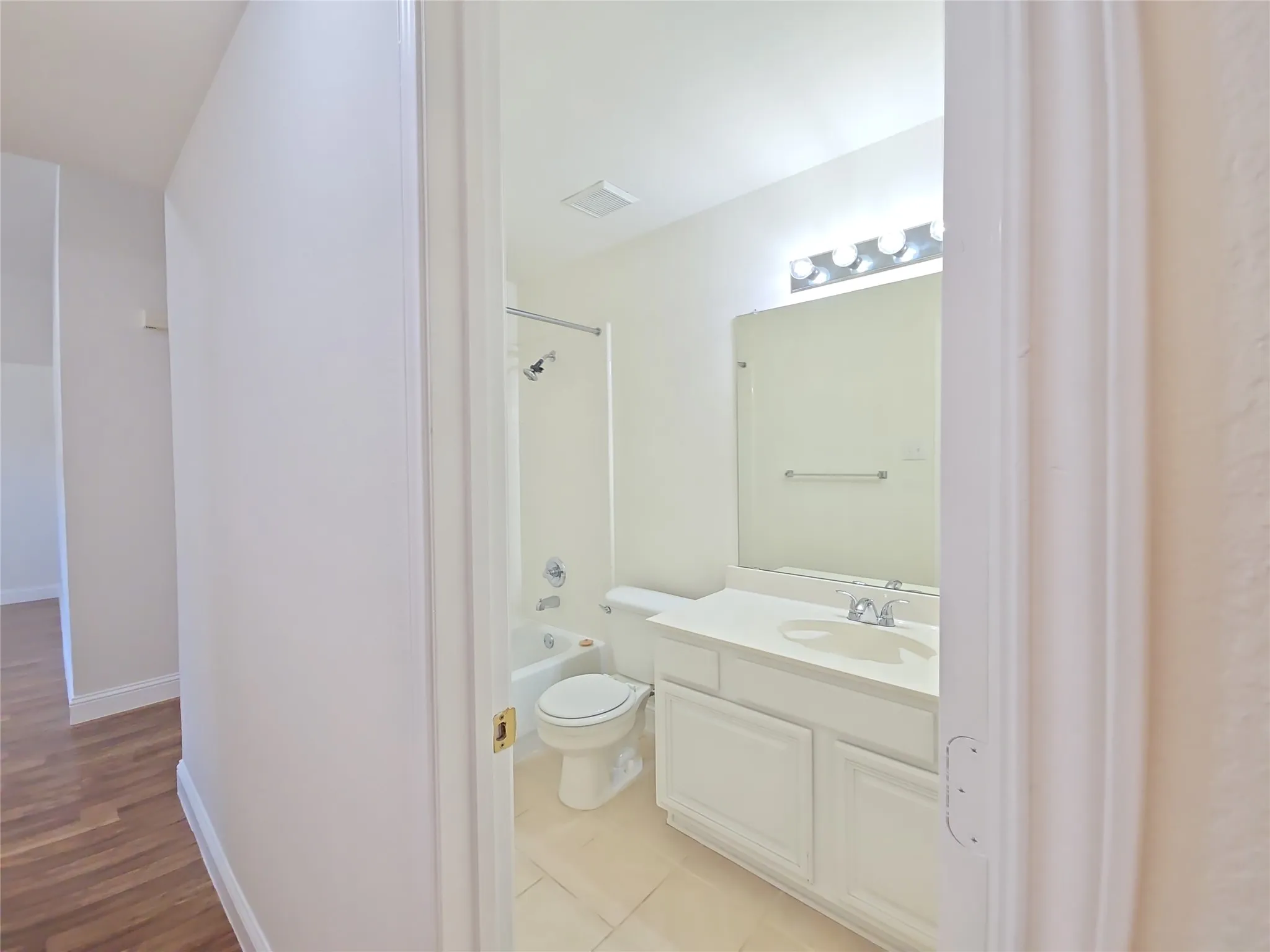 Bathroom featuring a single-sink vanity with white cabinetry, a built-in bathtub with shower, and tiled flooring