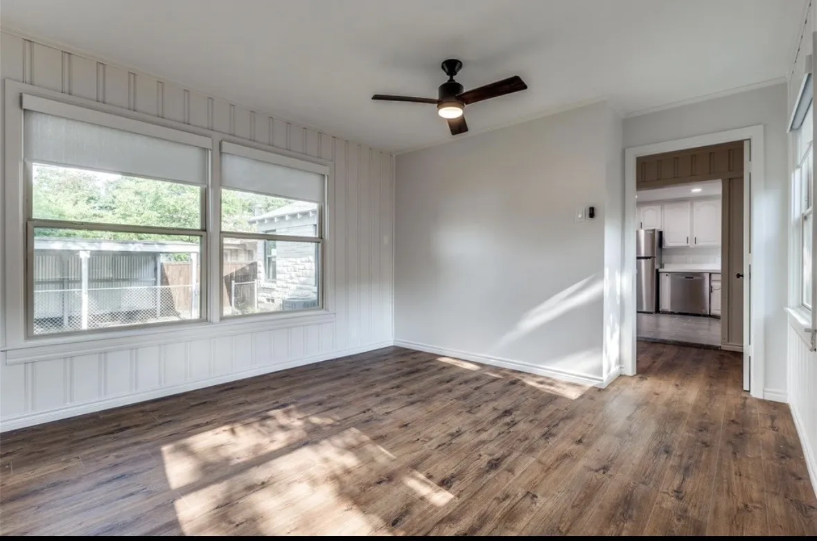 Wood-finish flooring, white paneled walls, a ceiling fan with integrated lighting, and multiple windows with roller shades