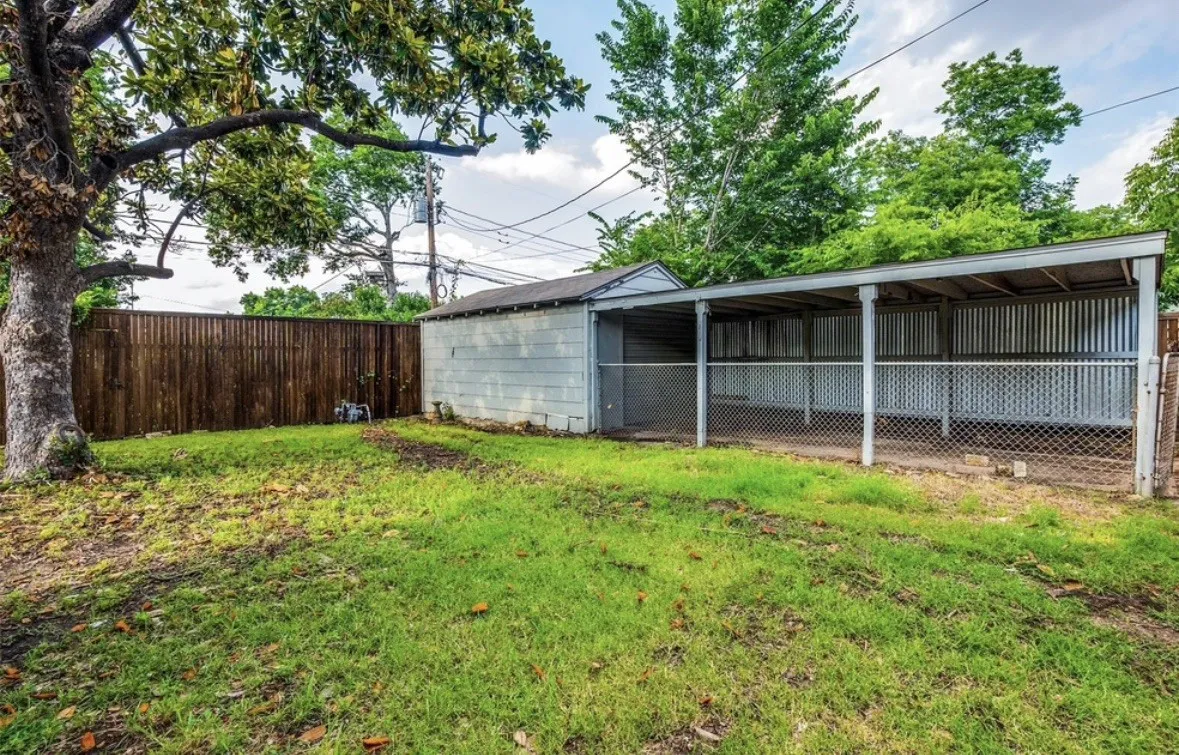 Expansive backyard featuring a wood privacy fence, mature trees, and a covered outbuilding with corrugated metal siding and chain-link fencing