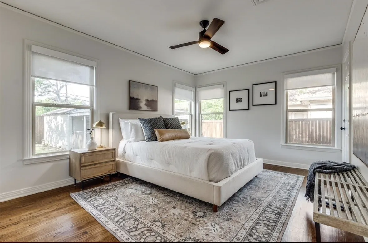Wood-finish flooring, multiple windows with roller shades, ceiling fan with light, and light-toned wall paint