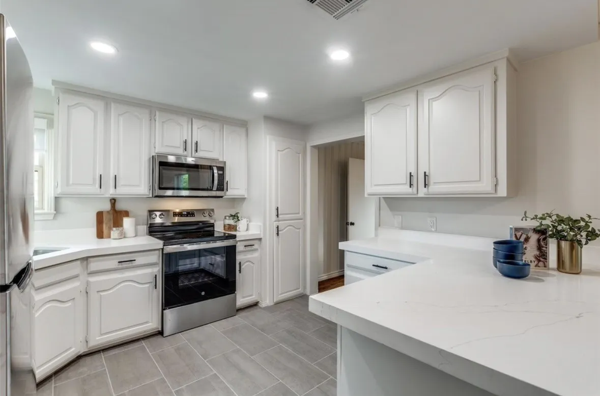 White cabinetry with black hardware, stainless steel appliances, solid surface countertops, recessed lighting, and tile flooring