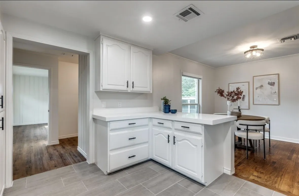 White cabinetry with black hardware, light-toned countertops, tile flooring, wood-finish flooring, and a window providing natural light