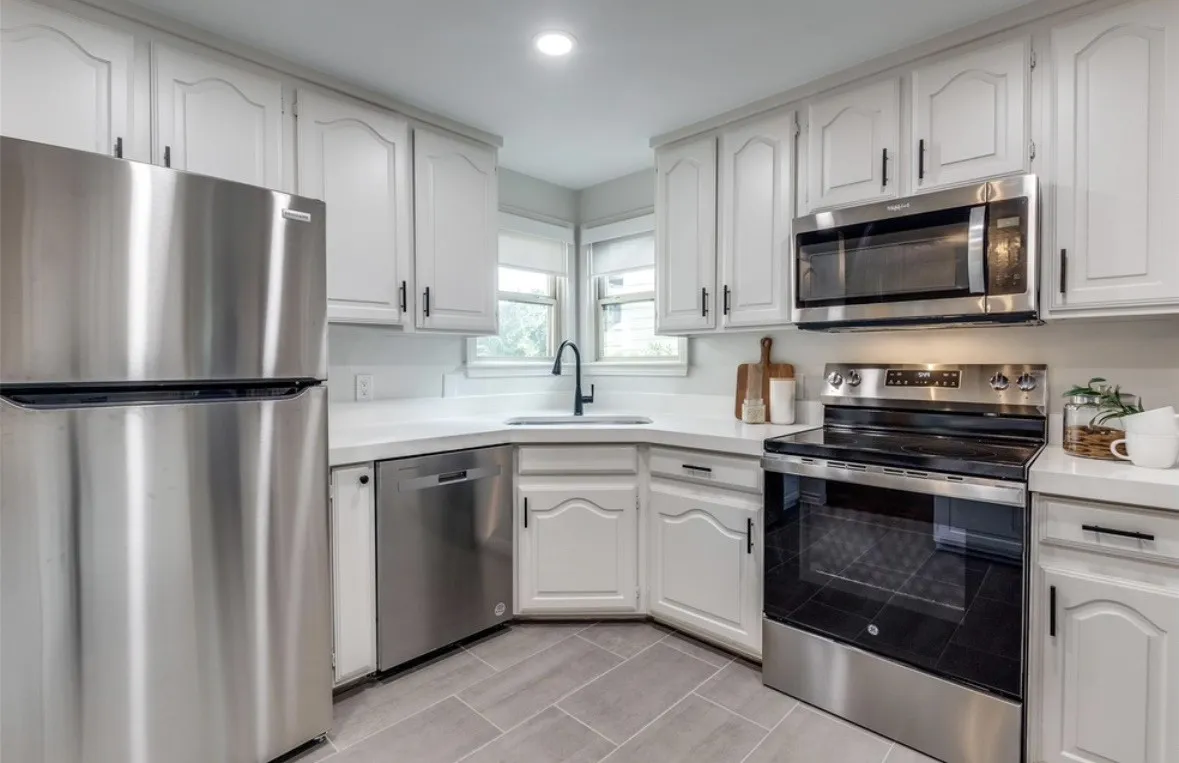 White cabinetry with black hardware, stainless steel appliances, light countertops, subway tile backsplash, and grey tile flooring