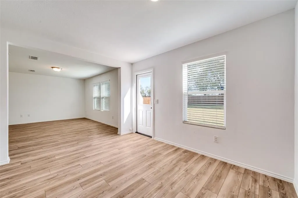 Open-concept living space featuring wood-finish flooring, white walls, and a prominent window with blinds