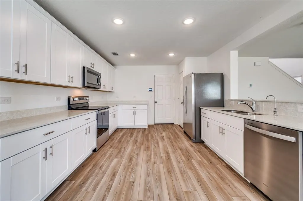 White shaker cabinetry, stainless steel appliances, wood-finish flooring, recessed lighting, and light-toned countertops
