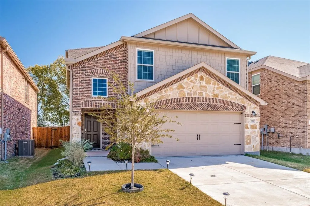 Brick and stone facade with a gable roofline, attached two-car garage, covered entry, and front landscaping