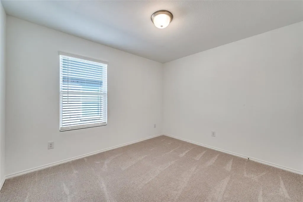 Neutral-toned walls, carpeted flooring, and a single window with horizontal blinds