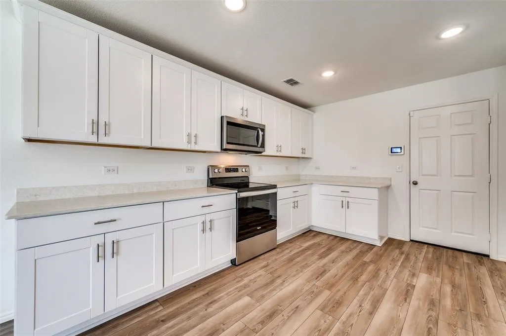 White shaker-style cabinetry with brushed nickel hardware, light-toned countertops, stainless steel appliances, and wood-finish flooring