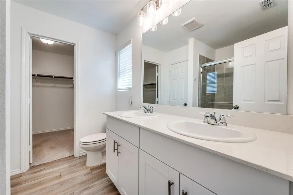 Dual vanity with white cabinetry and chrome hardware, white solid surface countertop, and wood-finish flooring