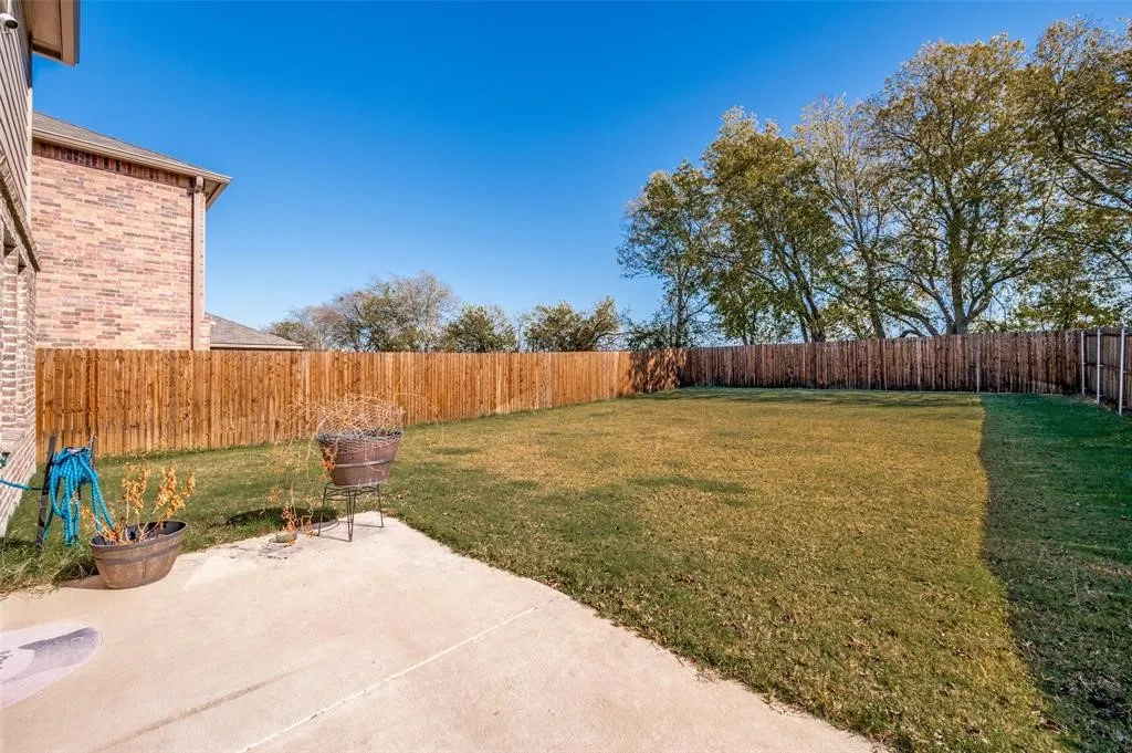 Expansive backyard with a concrete patio, wood privacy fence, and mature trees