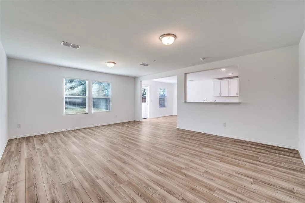 Wood-finish flooring throughout, two windows with blinds, and a pass-through opening to an adjacent room with white cabinetry