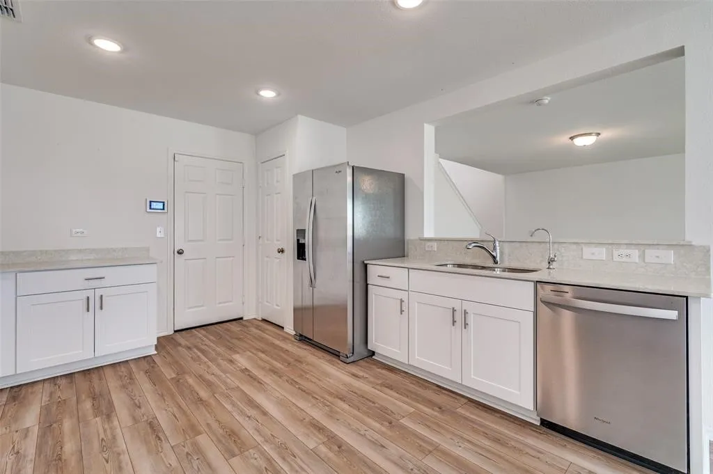 Wood-finish flooring with white cabinetry, light-toned countertops, and stainless steel appliances