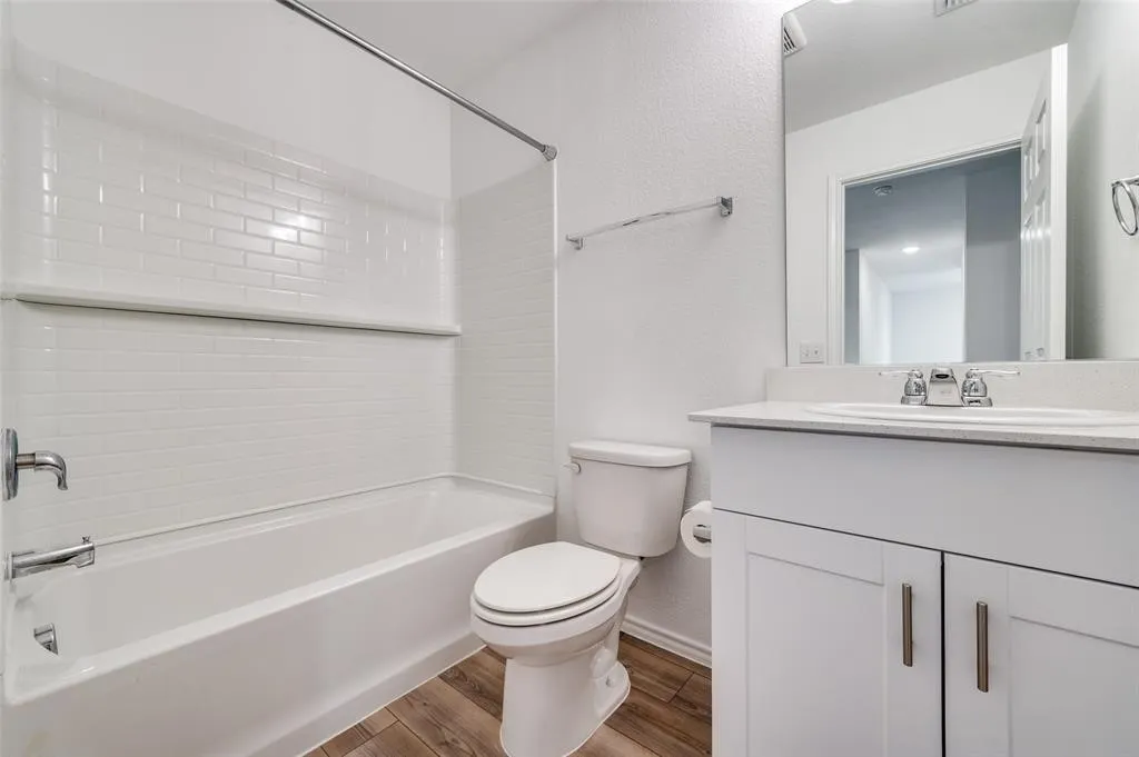 Tub and shower combination featuring subway tile surround, single vanity with integrated sink, white cabinetry with silver-tone hardware, and wood-finish flooring