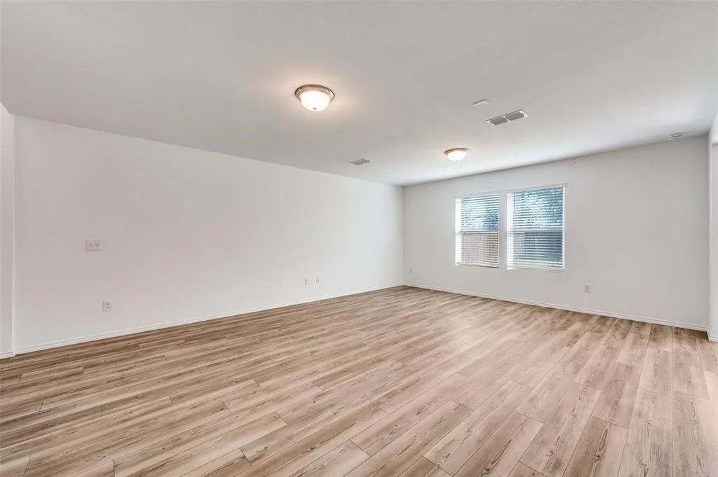Expansive room featuring wood-finish flooring, white walls, multiple windows with blinds, and flush-mount ceiling lighting