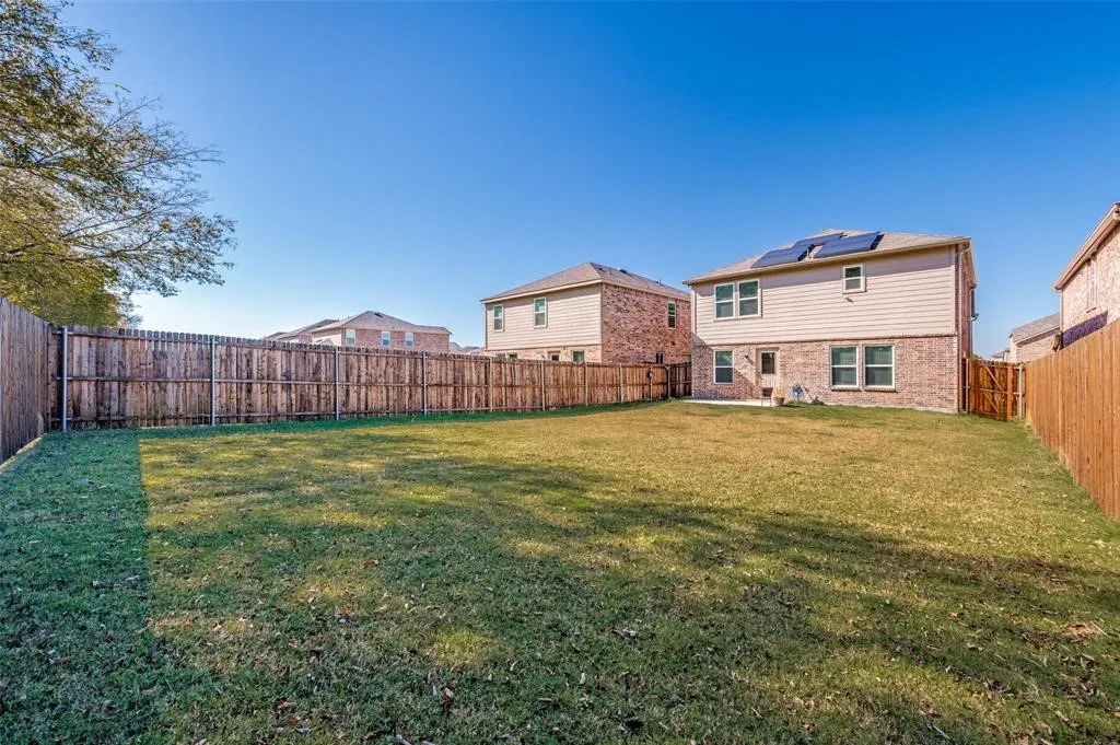 Expansive backyard with a manicured lawn, full privacy fencing, and a two-story brick and siding exterior