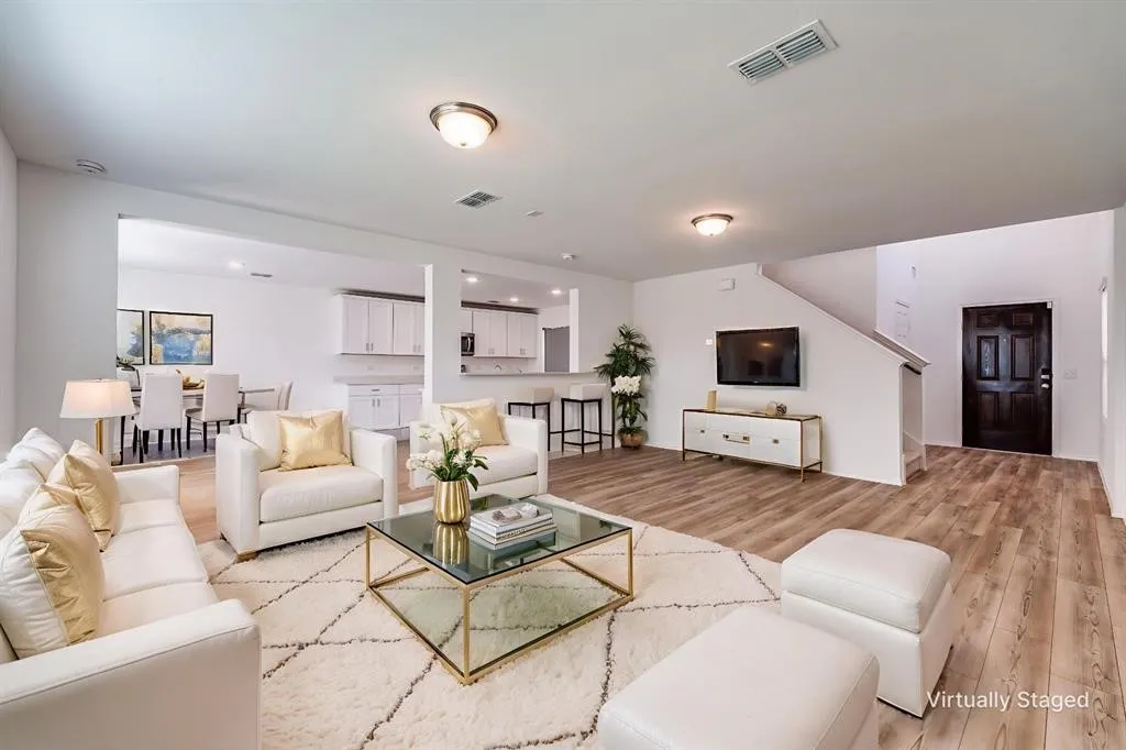 Wood-finish flooring throughout the main living areas, a staircase with a white railing, and a dark-paneled entry door
