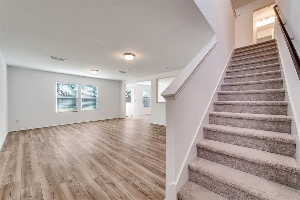 Spacious interior featuring wood-finish flooring, multiple windows, and a carpeted staircase with a dark wood handrail