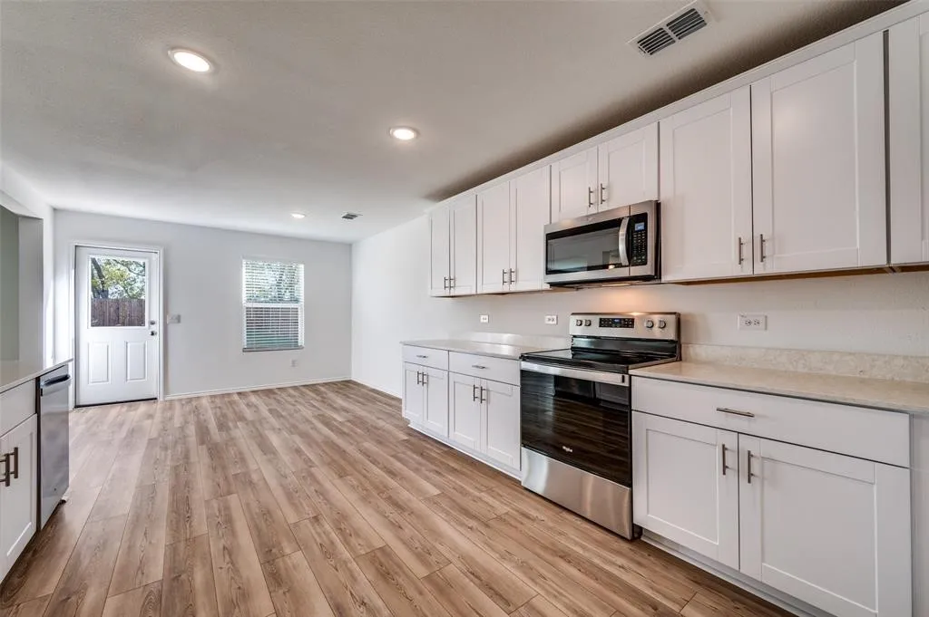 Open-concept kitchen with wood-finish flooring, white cabinetry, integrated stainless steel appliances, and light-toned countertops