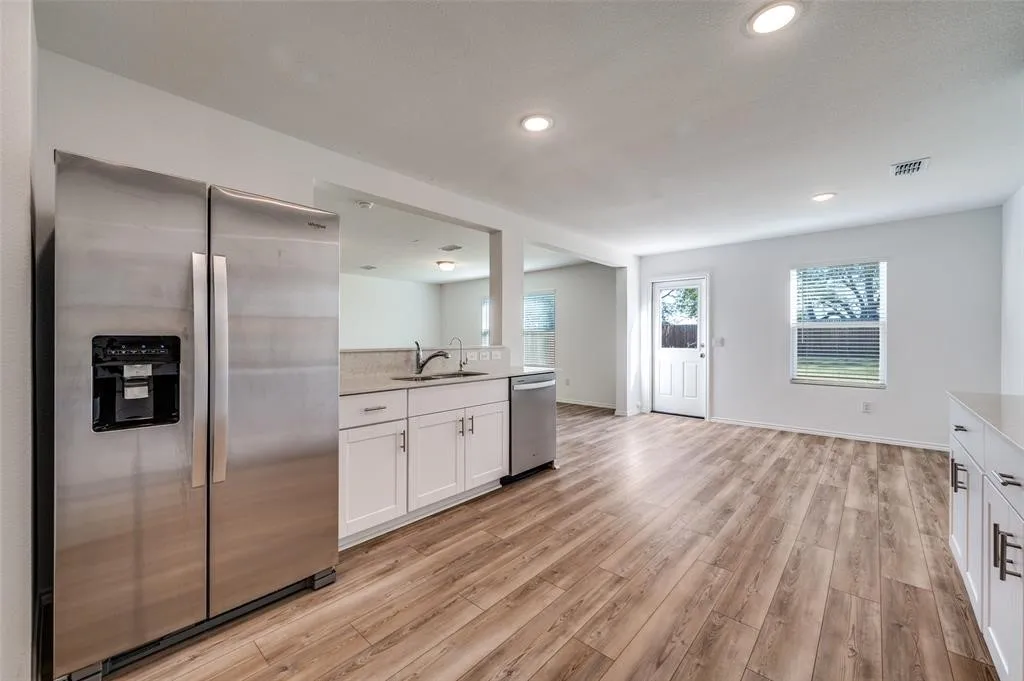 Wood-finish flooring throughout, recessed lighting, white cabinetry with silver hardware, stainless steel appliances, and a pass-through window