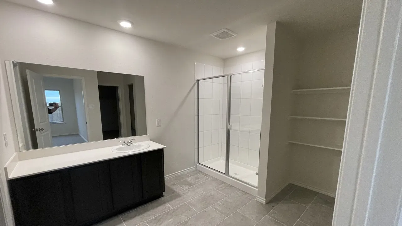 Spacious bathroom featuring a glass-enclosed shower, a vanity with a single sink and dark cabinetry, and built-in shelving