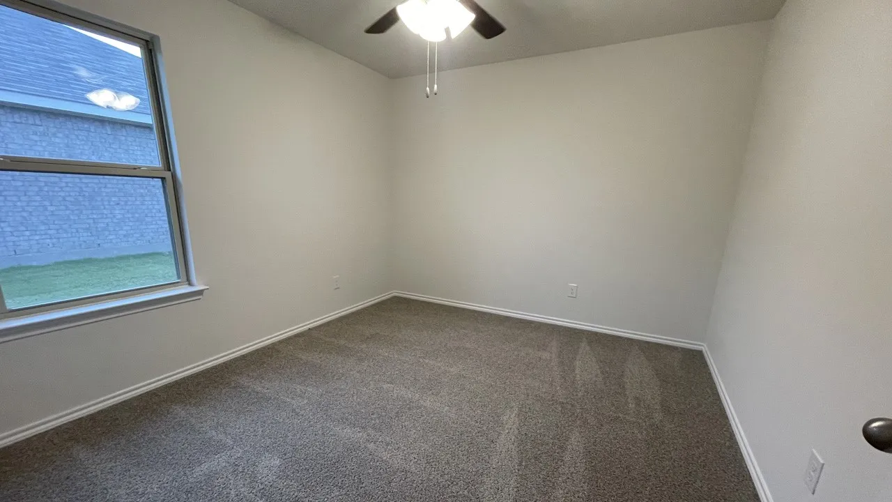 Neutral wall paint with textured carpeting, a ceiling fan with integrated lighting, and a double-paned window