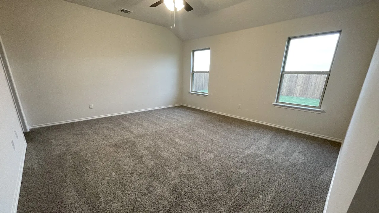 Vaulted ceiling, ceiling fan with light fixture, two windows, wall-to-wall carpeting, and neutral paint palette