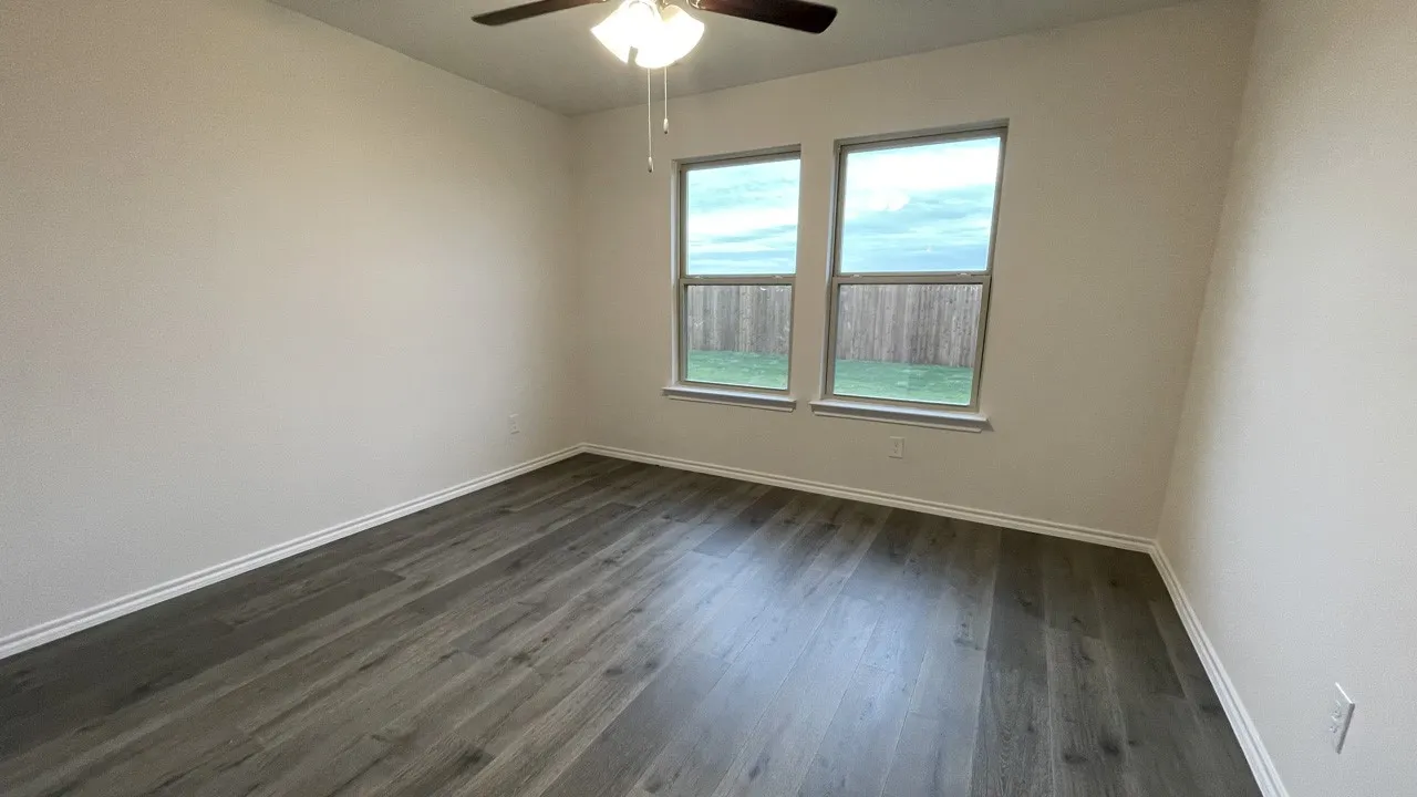 Wood-finish flooring with white trim, two windows, and a ceiling fan
