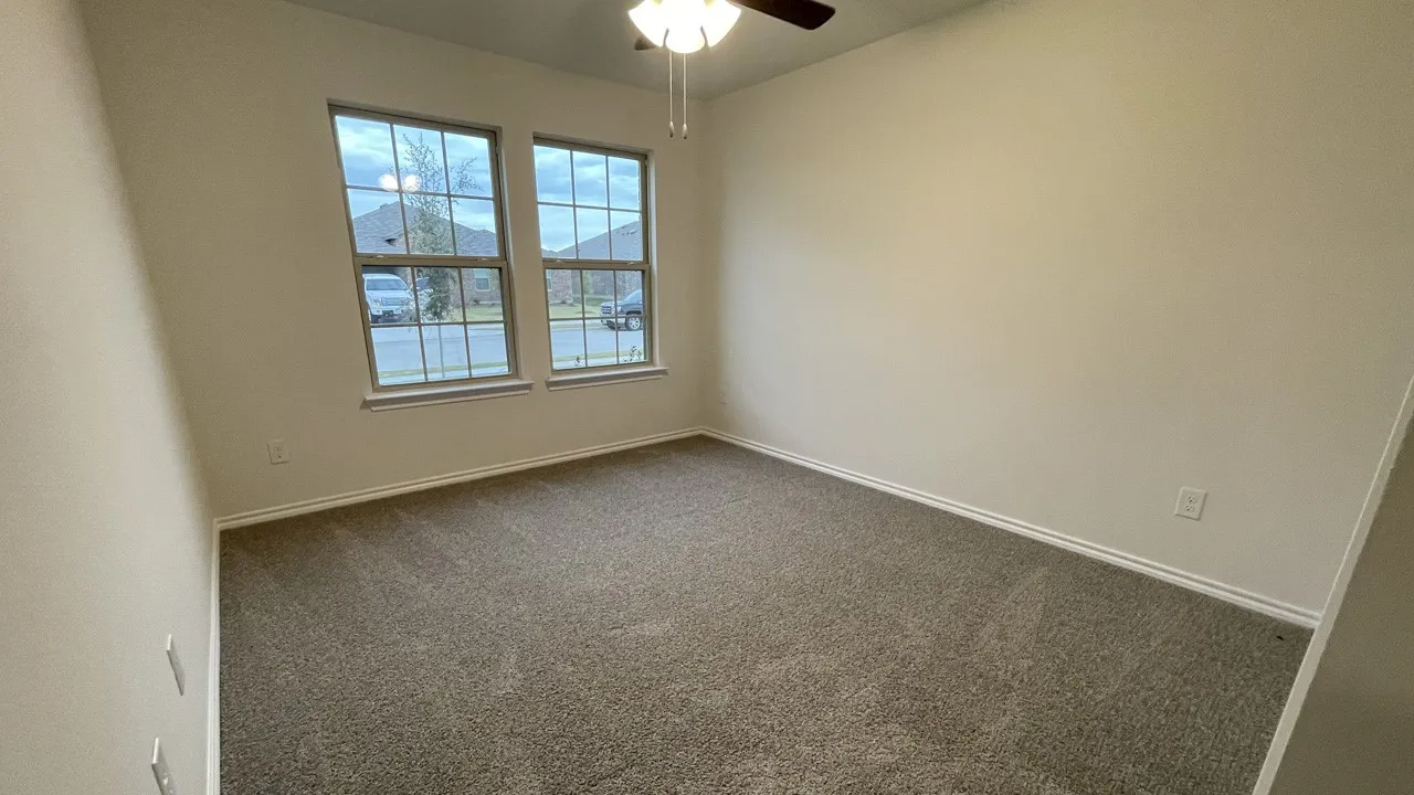 Plush carpet flooring, neutral wall paint, two large windows, and a ceiling fan