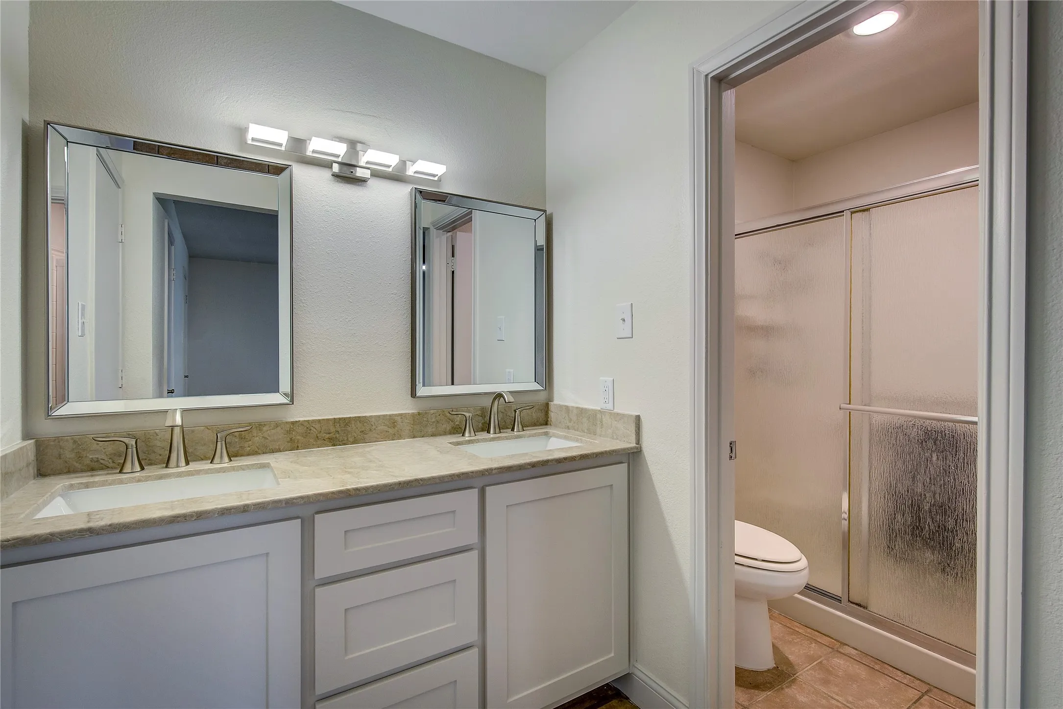 Primary bathroom has new double sink vanity, lighting and faucets, and glass-door shower.