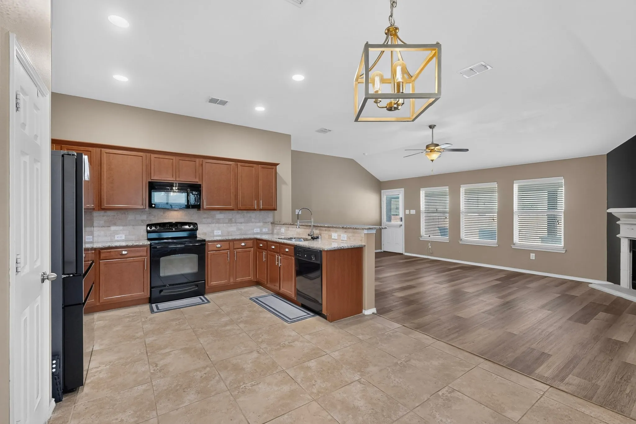 Open-concept kitchen with wood cabinetry, black appliances, and a tiled backsplash