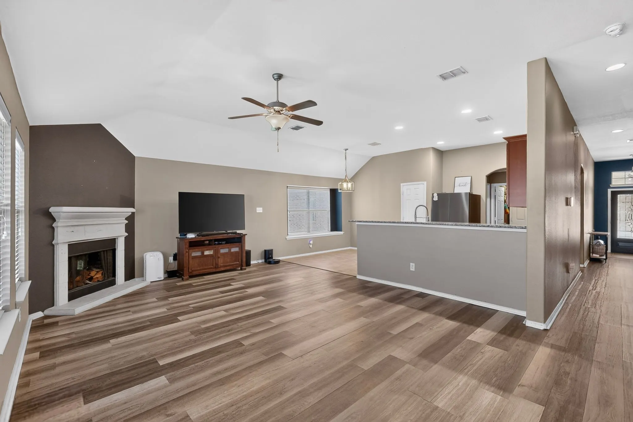 Open-concept living area featuring wood-finish flooring, a white mantel fireplace, and a ceiling fan