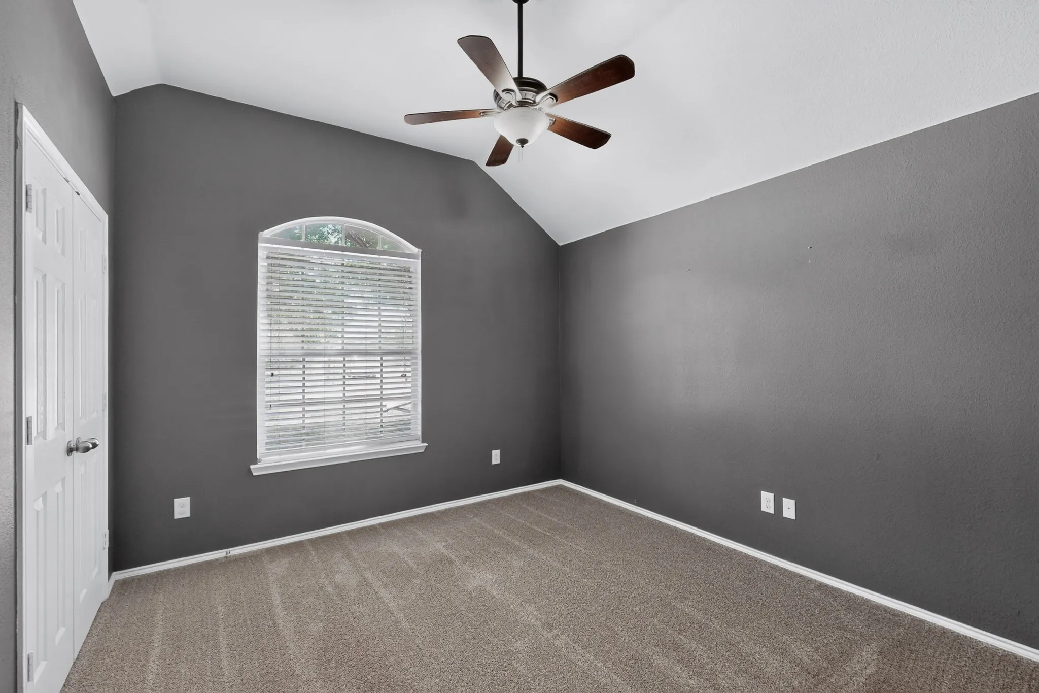 Vaulted ceiling with a ceiling fan, arched window with blinds, paneled door, and carpeted flooring